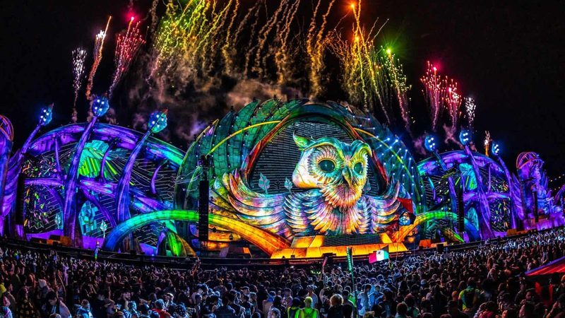 The EDC main stage lit up at night with the festival crowd in front of it.