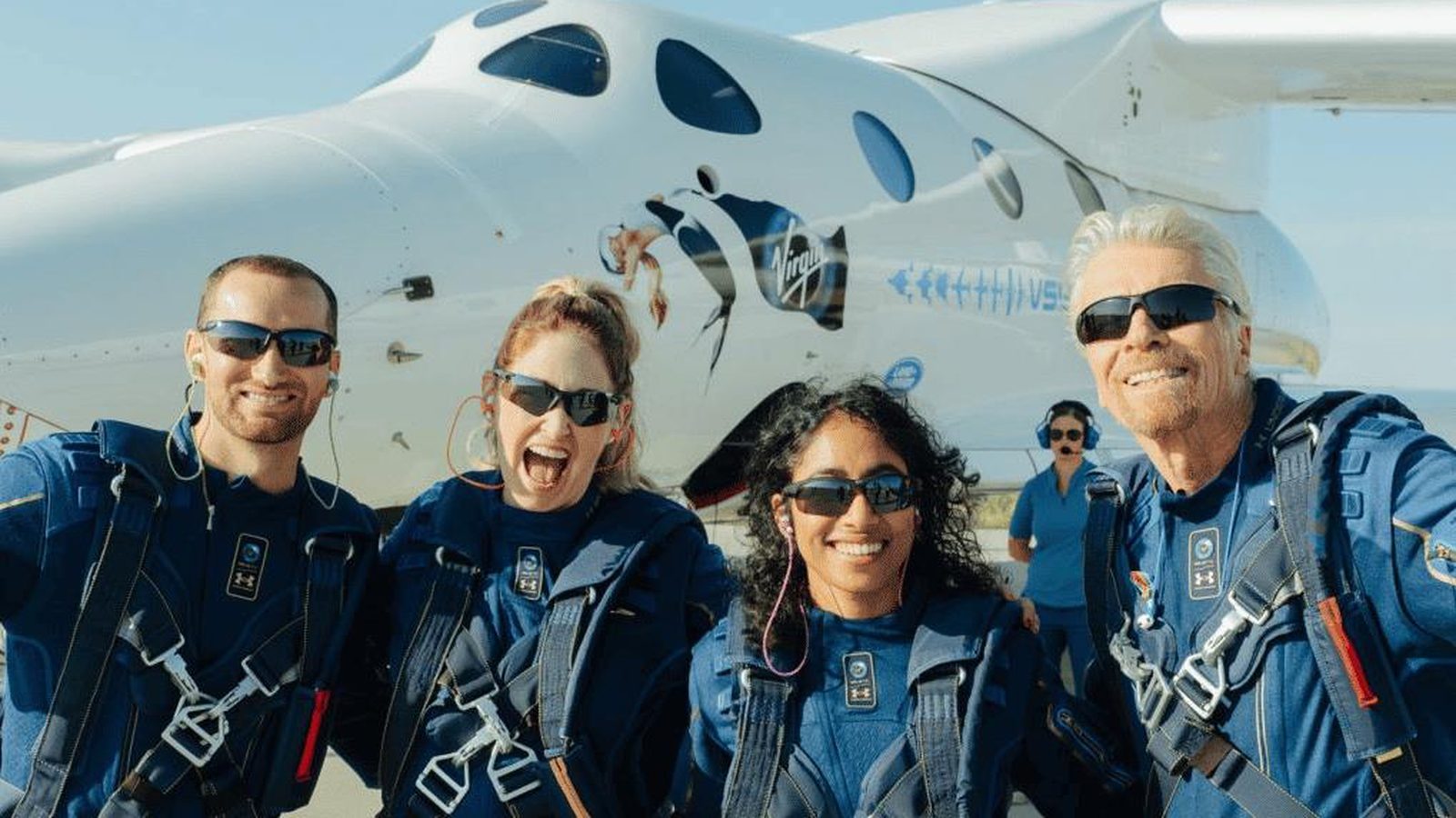 The Unity 22 crew, including Richard Branson, in flight suits in front of the spacecraft after landing.